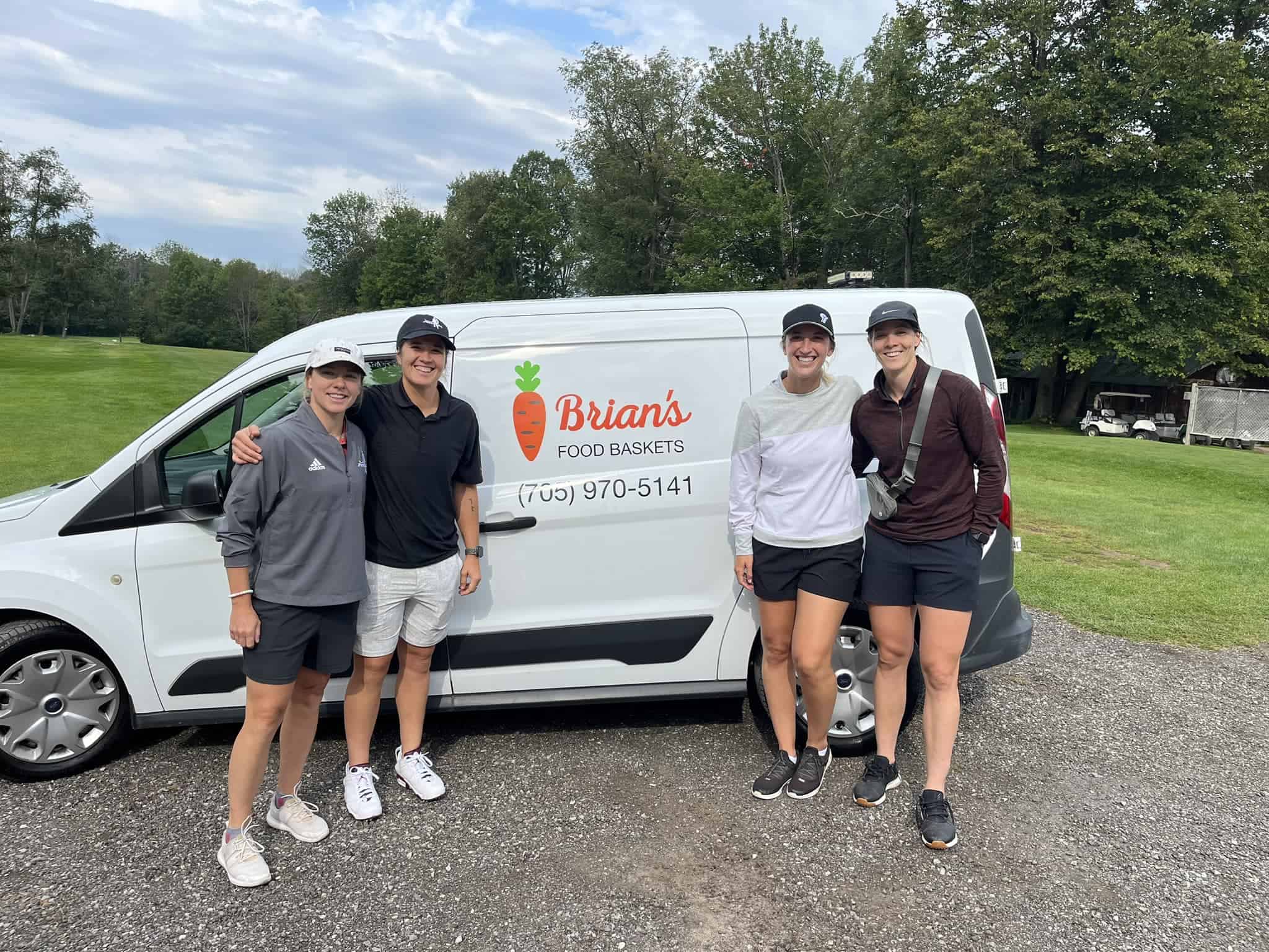 Four people standing beside the Brian's Food Baskets delivery van